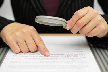 Person holding a magnifying glass and pointing at text on a document, closely examining the content.