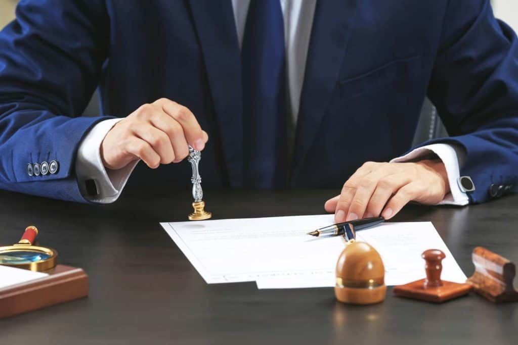 Person in a suit stamping a document on a desk with other stamps and a magnifying glass.